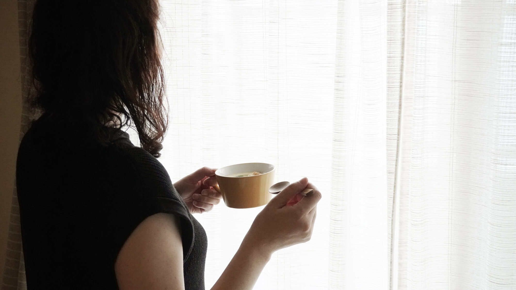 窓辺で茶碗蒸しを味わう女性